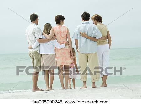 Stock Photograph - Group standing near edge of water on beach, rear view. Fotosearch