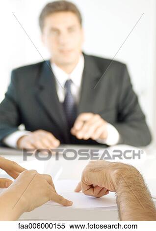 Stock Photography - Hands pointing to document, salesman in background. Fotosearch