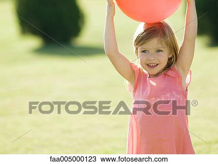 Stock Image - Little girl holding ball on head. Fotosearch