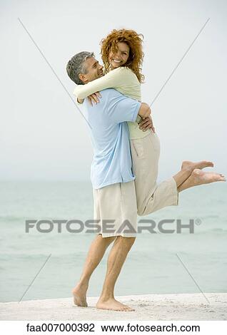 Stock Image - Man holding woman on beach. Fotosearch