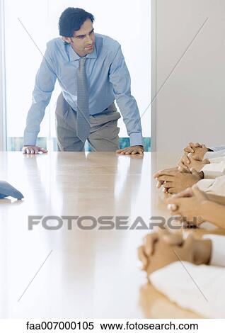 Man leaning on meeting table, looking toward team View Large Photo Image Stock Photography - Man leaning on meeting table, looking toward team. Fotosearch