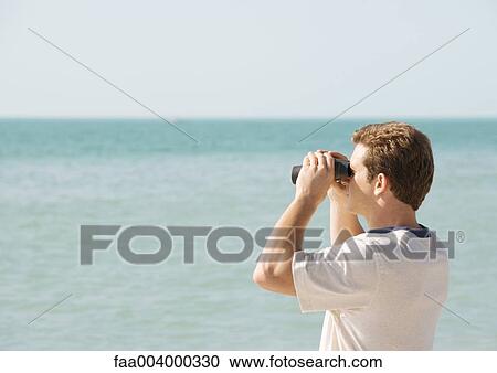 Stock Image - Man looking out to sea with binoculars. Fotosearch