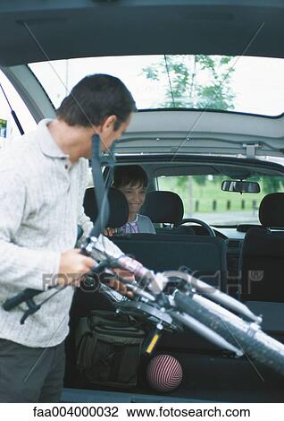 Stock Image - Man putting bike into car trunk. Fotosearch