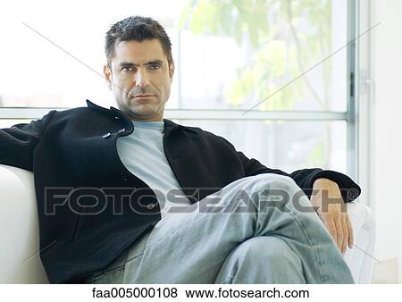 Man sitting on sofa with legs crossed, portrait View Large Photo Image Stock Photo - Man sitting on sofa with legs crossed, portrait. Fotosearch