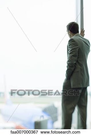 Man standing by window in airport View Large Photo Image Stock Photo - Man standing by window in airport. Fotosearch