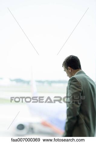 Stock Photo - Man standing by window in airport. Fotosearch