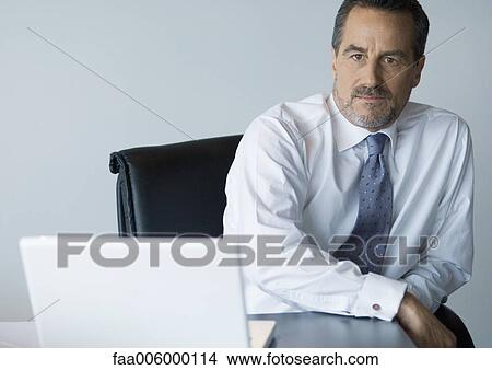 Mature businessman sitting at desk, frowning View Large Photo Image Picture - Mature businessman sitting at desk, frowning. Fotosearch