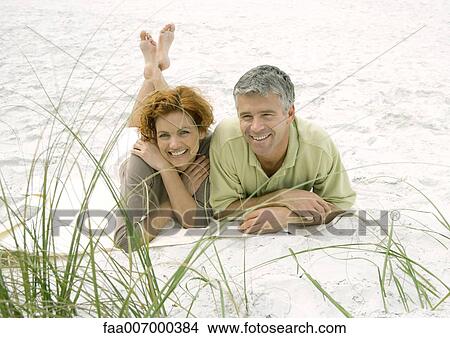 Picture - Mature couple lying on beach, front view. Fotosearch