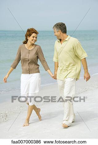 Stock Photograph - Mature couple walking barefoot on beach. Fotosearch