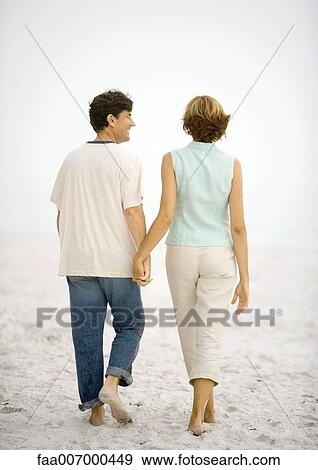 Mature couple walking hand in hand on beach, rear view View Large Photo Image Stock Photo - Mature couple walking hand in hand on beach, rear view. Fotosearch