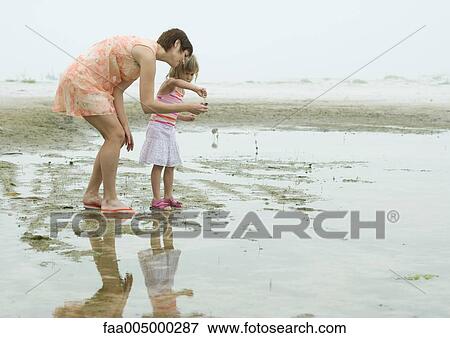 Stock Photo - Mother and daughter on beach, full length. Fotosearch