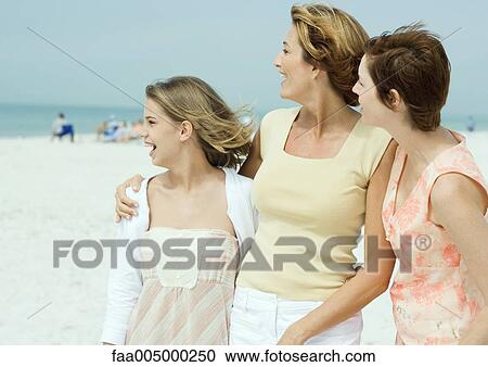 Stock Image - Mother with teenage daughter and friend on beach, looking toward distance. Fotosearch