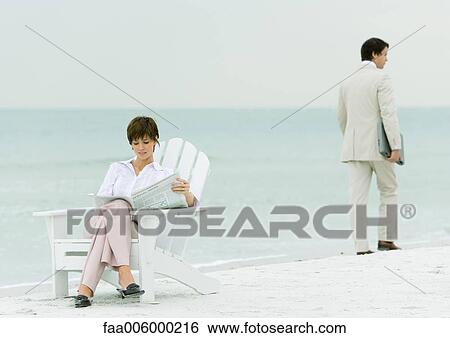 On beach, businessman carrying laptop, walking by woman reading newspaper in chair View Large Photo Image Stock Photograph - On beach, businessman carrying laptop, walking by woman reading newspaper in chair. Fotosearch