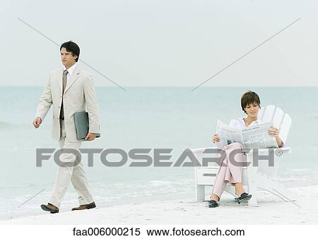 On beach, businessman carrying laptop, walking by woman reading newspaper in chair View Large Photo Image Stock Photography - On beach, businessman carrying laptop, walking by woman reading newspaper in chair. Fotosearch