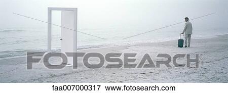 Stock Photo - On beach, businessman with suitcase looking over shoulder at open doorway. Fotosearch