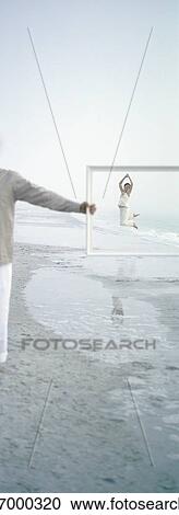 On beach, woman jumping in distance, seen through frame held by man View Large Photo Image Stock Image - On beach, woman jumping in distance, seen through frame held by man. Fotosearch