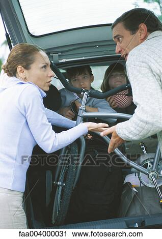 Stock Image - Parents putting bike into car trunk and arguing while children watch from car. Fotosearch