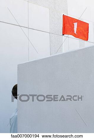 Part of man visible behind wall and red flag with number "1" overhead View Large Photo Image Picture - Part of man visible behind wall and red flag with number "1" overhead. Fotosearch