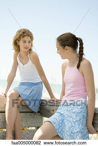 Stock Image - Preteen girls sitting on railing talking in beach setting. Fotosearch