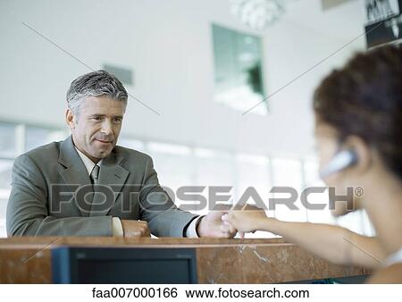 Stock Photograph - Receptionist handing something to man across counter. Fotosearch