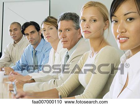 Stock Image - Row of business people sitting at table. Fotosearch