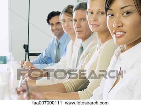 Stock Image - Row of business people sitting at table. Fotosearch