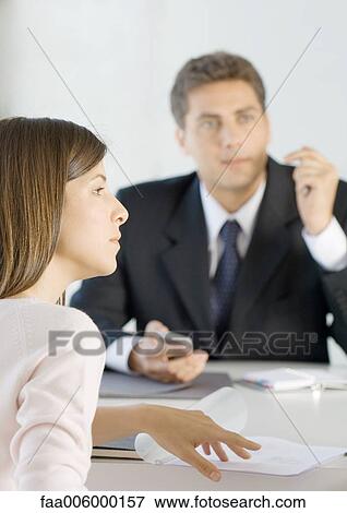 Salesman and woman sitting at table with documents, looking out of frame View Large Photo Image Stock Photo - Salesman and woman sitting at table with documents, looking out of frame. Fotosearch