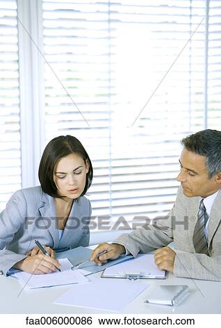 Two business associates discussing documents at desk View Large Photo Image Stock Photograph - Two business associates discussing documents at desk. Fotosearch