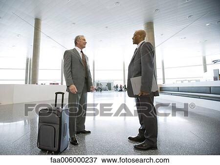 Two businessman standing talking in airport concourse View Large Photo Image Stock Photo - Two businessman standing talking in airport concourse. Fotosearch