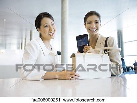 Two businesswoman smiling, one holding purse, the other holding up passport View Large Photo Image Stock Image - Two businesswoman smiling, one holding purse, the other holding up passport. Fotosearch