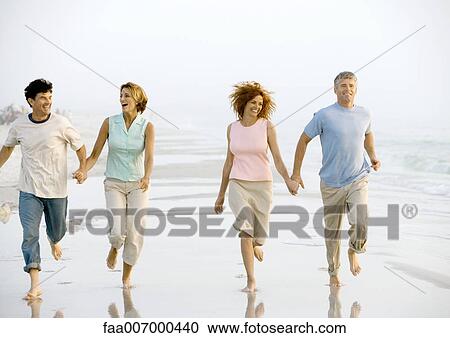 Stock Image - Two mature couples running on beach. Fotosearch
