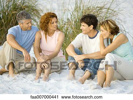 Stock Image - Two mature couples sitting on beach, talking. Fotosearch