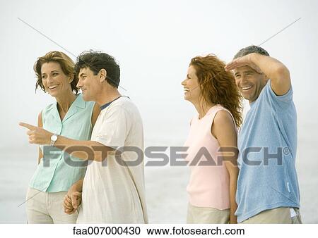 Stock Image - Two mature couples standing on beach. Fotosearch
