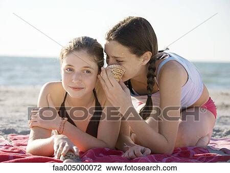 Stock Image - Two preteen girls whispering on beach. Fotosearch