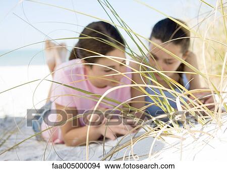 Two teenage girls lying on beach, seen through dune grass View Large Photo Image Picture - Two teenage girls lying on beach, seen through dune grass. Fotosearch