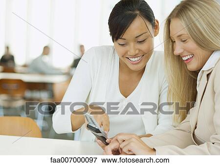 Stock Photo - Two young business women looking at cell phone together. Fotosearch