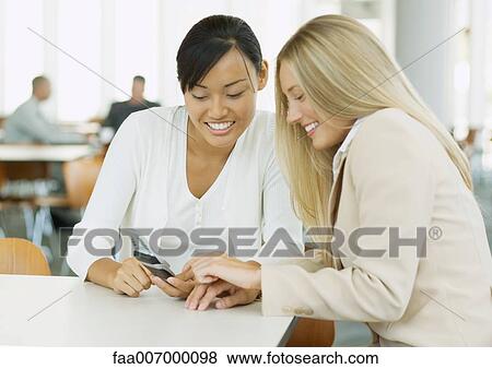 Two young business women looking at cell phone together View Large Photo Image Stock Photo - Two young business women looking at cell phone together. Fotosearch