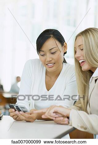 Two young business women looking at cell phone together View Large Photo Image Stock Photo - Two young business women looking at cell phone together. Fotosearch