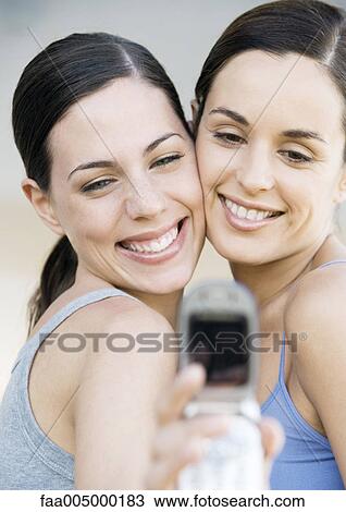 Two young female friends, cheek to cheek, taking photo with cell phone View Large Photo Image Stock Image - Two young female friends, cheek to cheek, taking photo with cell phone. Fotosearch