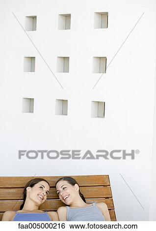 Two young women reclining and talking side by side View Large Photo Image Stock Photograph - Two young women reclining and talking side by side. Fotosearch