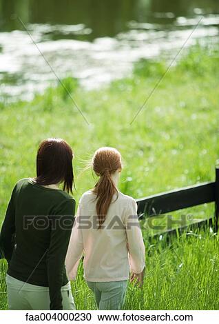 Woman and girl walking along wooden fence, pond in background View Large Photo Image Stock Image - Woman and girl walking along wooden fence, pond in background. Fotosearch