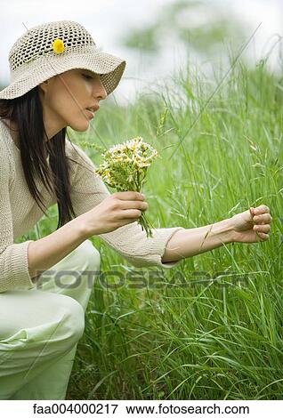 Stock Photo - Woman crouching in long grass, holding bunch of flowers. Fotosearch