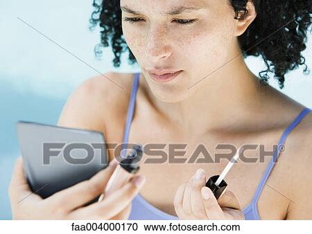 Woman holding lip gloss and looking in mirror View Large Photo Image Stock Image - Woman holding lip gloss and looking in mirror. Fotosearch