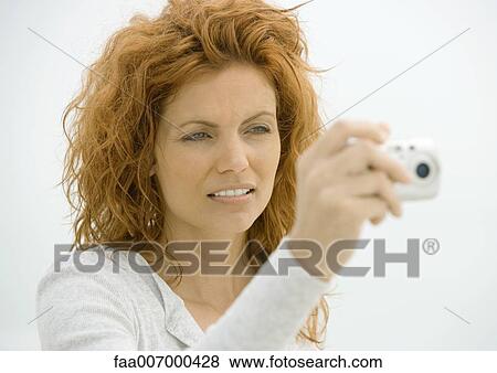 Stock Photo - Woman holding up camera, squinting. Fotosearch