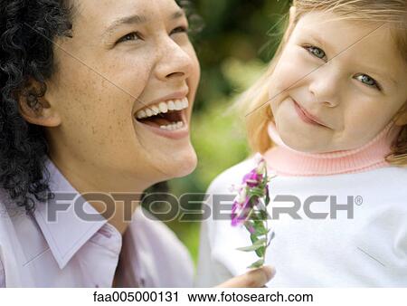 Stock Image - Woman laughing and holding flower, next to little girl. Fotosearch