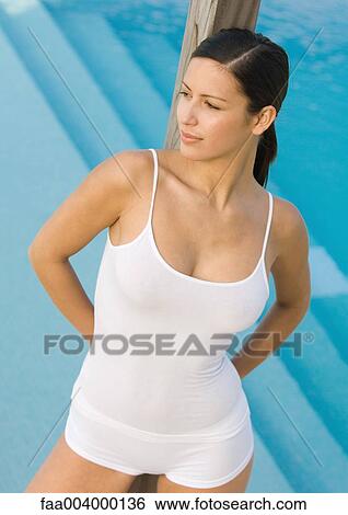Stock Photograph - Woman leaning against wooden pole, swimming pool in background. Fotosearch