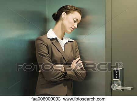 Stock Image - Woman leaning head against wall next to door. Fotosearch