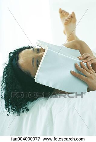 Woman lying in bed, covering face with book View Large Photo Image Stock Photo - Woman lying in bed, covering face with book. Fotosearch