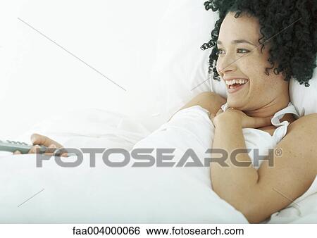 Woman lying in bed, holding remote control View Large Photo Image Stock Photograph - Woman lying in bed, holding remote control. Fotosearch