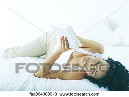 Stock Photo - Woman lying in bed with book. Fotosearch